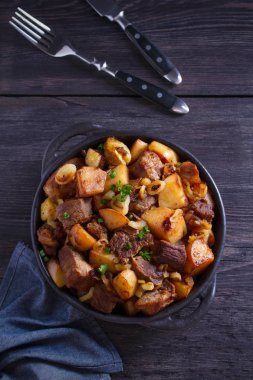 Soğan ve sarımsak ile kızarmış sığır eti ve patates ahşap arka plan üzerinde siyah çanak servis