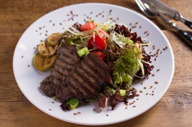 Sığır salatası: domates, salatalık, kabak, marul ve lahana ile ızgara sığır biftek, keten tohumu serpilir. Ev yapımı yemekler. Lezzetli ve sağlıklı bir yemek için konsept
