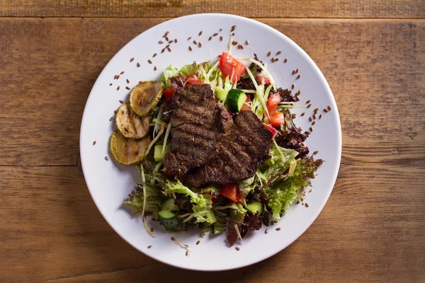 Beef salad: grilled beef steaks with tomatoes, cucumbers, zucchini, lettuce and cabbage, sprinkled with flax seeds. View from above, top studio shot
