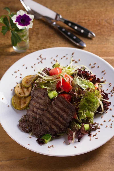 Beef salad: grilled beef steaks with tomatoes, cucumbers, zucchini, lettuce and cabbage, sprinkled with flax seeds. Home made food. Concept for a tasty and healthy meal