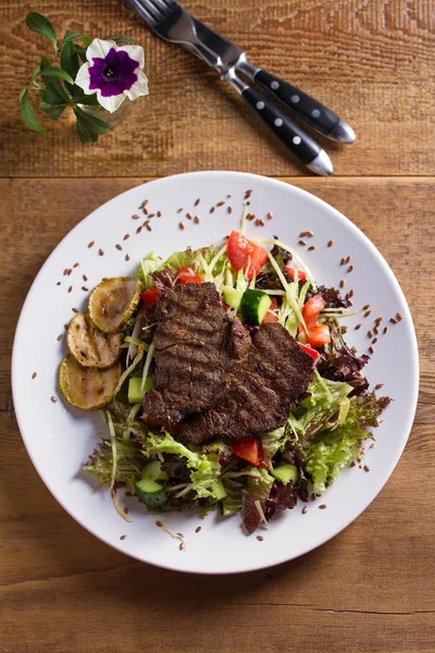 Beef salad: grilled beef steaks with tomatoes, cucumbers, zucchini, lettuce and cabbage, sprinkled with flax seeds. View from above, top studio shot