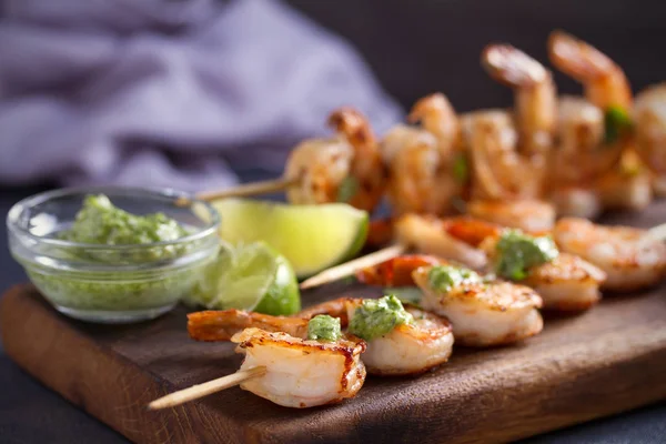 Skewered shrimps with garlic butter sauce served with cilantro and lime on serving board