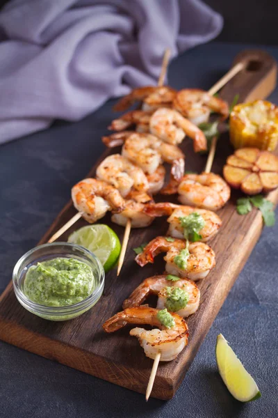 Skewered shrimps with garlic butter sauce served with cilantro and lime on serving board