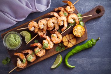 Sarımsak tereyağı soslu şiş karides ler servis tahtasında kişniş ve kireç ile servis edilir