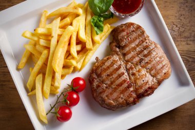 Beyaz tabakta patates kızartması, sos ve sebze ile ızgara domuz biftek