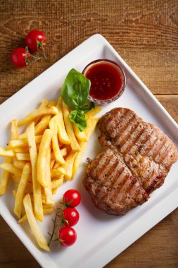 Beyaz tabakta patates kızartması, sos ve sebze ile ızgara domuz biftek