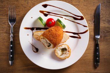 Tavuk Kiev ve beyaz plaka, ahşap arka plan üzerinde sebze. Ekmekli tavuk göğsü otlar ve tereyağı ile doldurulmuş