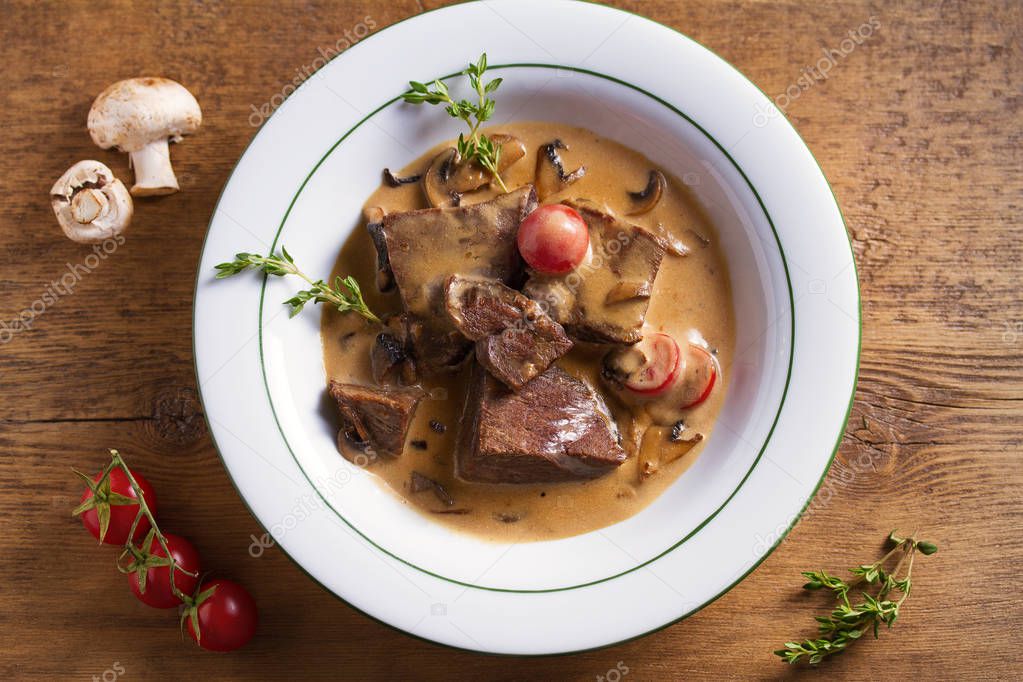 Braised veal cheeks in cream sauce with mushrooms. View from above, top studio shot 