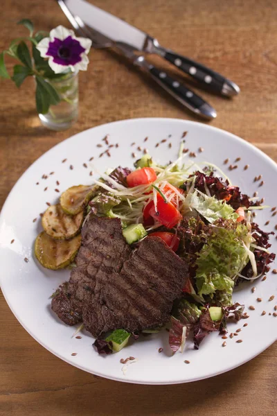 Beef salad: grilled beef steaks with tomatoes, cucumbers, zucchini, lettuce and cabbage, sprinkled with flax seeds. Vertical image