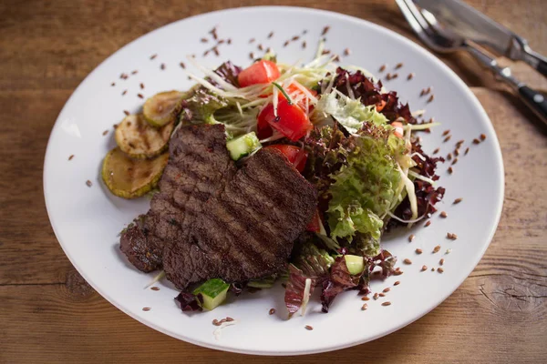 Beef salad: grilled beef steaks with tomatoes, cucumbers, zucchini, lettuce and cabbage, sprinkled with flax seeds. Horizontal image