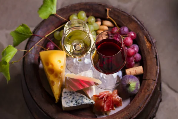 Red and white wine with  grapes on old cask in wine cellar. Glasses and bottles of wine with cheese, jamon, figs and nuts. View from above, top view