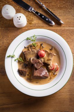 Krema soslu ağır ateşte pişmiş sığır yanakları ve mantarlı domatesler ahşap masada beyaz kasede. Genel giderler