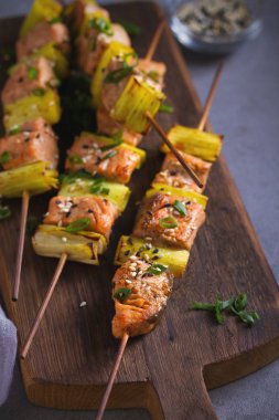 Teriyaki soslu şiş somon pırasası, servis panosuna susam tohumu serpiştirilmiş. Dikey resim