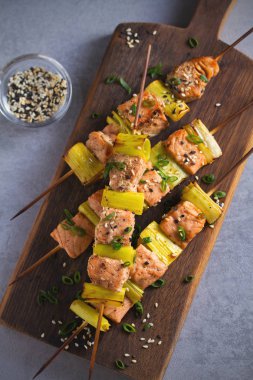 Teriyaki soslu şiş somon pırasası, servis panosuna susam tohumu serpiştirilmiş. Genel, dikey