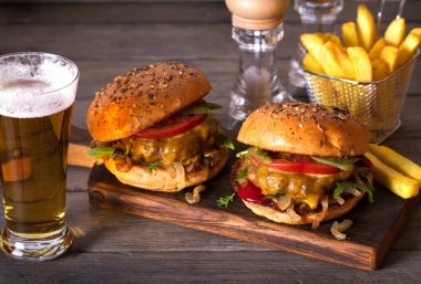 Klasik Amerikan usulü sığır köftesi, üstünde erimiş peynir, domates, soğan, sos ve bir bardak birayla servis edilen patates kızartması.