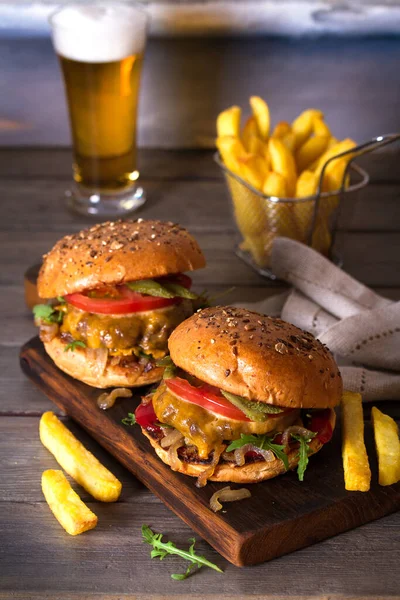 Beef burger in classic american style with hot grilled patty, melted cheese on top, tomato, onion, sauce and chips served with glass of beer