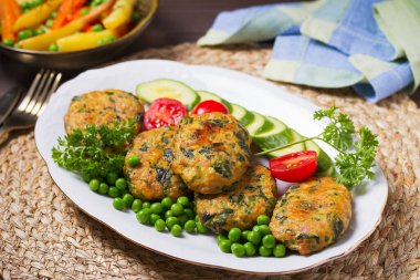 Beyaz tabakta yeşil bezelye ve sebzeli tavuk ıspanaklı burger.