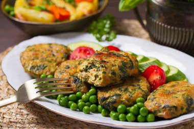 Beyaz tabakta yeşil bezelye ve sebzeli tavuk ıspanaklı burger.