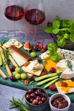 Çeşitli peynir çeşitleri var. Peynir seçimi. Üzüm, incir, fındık ve turşuyla servis edilen peynir tabağı. Şarap bardakları. Şarap için yiyecek.