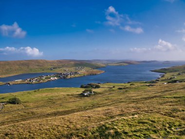 Mainland, Shetland, İskoçya, İngiltere 'nin batısındaki Weisdale Voe manzarası, güneşli bir günde mavi gökyüzü ile çekildi ve Kalliness' deki evler aydınlandı ve Hellister Gölü solda belirdi..