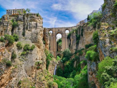 Güney İspanya 'nın Endülüs bölgesindeki Ronda kasabasındaki Puente Nuevo / Yeni Köprüsü, Guadalevn Nehri üzerinde 120 metre derinlikte bir uçurum oluşturarak, güneşli bir günde açık bulutlu bir havada çekildi..