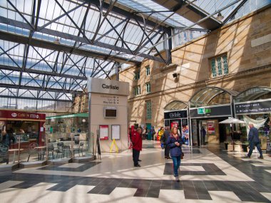 Güneşli bir öğleden sonra Carlisle Tren İstasyonu 'nun yolcuları, arka planda istasyon dükkanları
