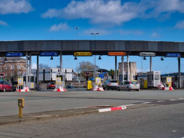 Arabalar, güneşli bir günde mavi gökyüzü eşliğinde Queensway Tüneli 'nin Birkenhead tarafında Mersey Nehri' nin altında Liverpool 'a giden gişelere yanaşıyor.
