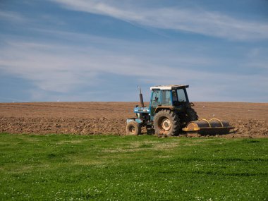 Bir çiftçi traktörle yeşil bir tarlayı sürüyor yazın sonunda sakin ve güneşli bir günde mahsul ekmeye hazırlanıyor..