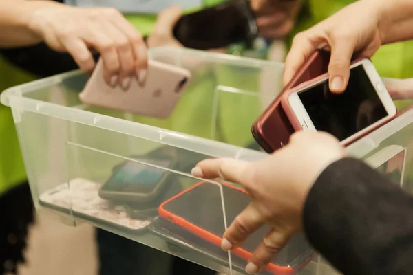İnsanlar cep telefonlarını şeffaf bir plastik kutuya koyuyorlar. Akıllı telefon kullanımına yasak