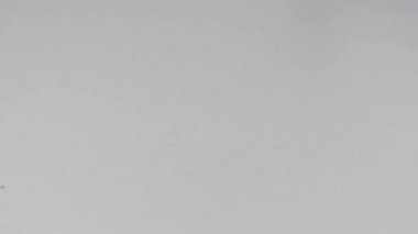 Bir mobilya zımbası için demir parlak klipsler beyaz bir masaya düşer ve yavaş çekimde zıplar. homojen arka plan. 180 fps