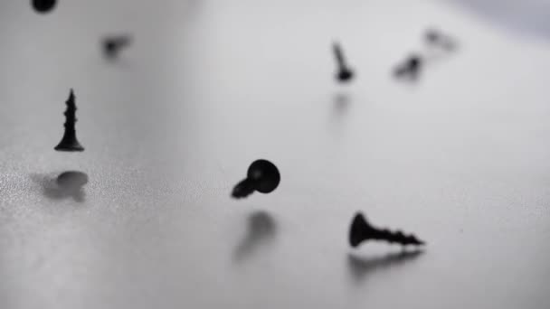 黒い鉄のネジが白いテーブルに落ちてゆっくりと動き出す 均質な背景 180Fps — ストック動画
