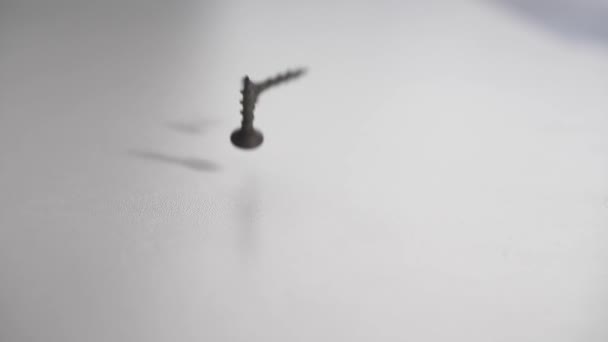 黒い鉄のネジが白いテーブルに落ちてゆっくりと跳ねる 均質な背景 180Fps — ストック動画