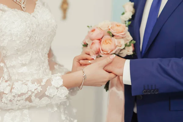 Gelin, düğün töreninde altın yüzüğü kocasının parmağına taktığında sevinçle gülümser. Kız büyük yakalı gri bir gelinlik giyiyor.