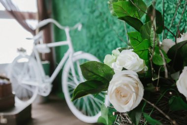 Yeşil duvarın arkasında duran bir bisikletin arka planında duran beyaz güller.