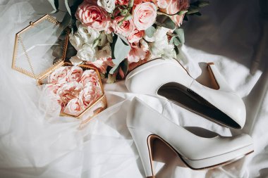 Altın renkli alyanslar, gelin buketi ve gelinlerin ayakkabılarının yanındaki dekoratif bir kutuda duruyor. metin eklenecek bir yer var