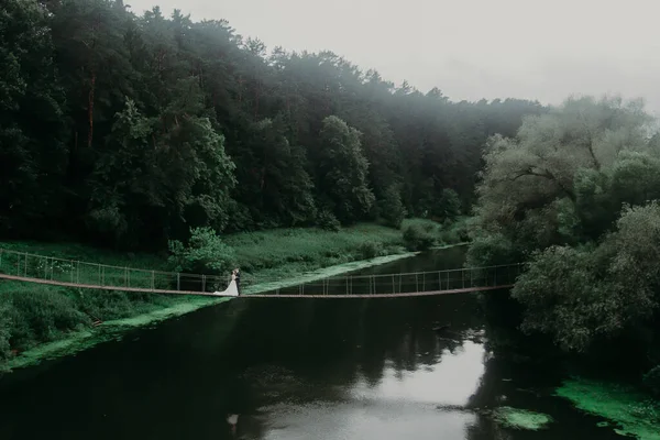 wedding couple kisses standing in the center of a sub-bridge over a large river. view from the drone from above. against a dark green forest