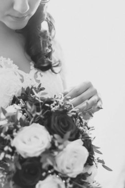 Gelin, beyaz güller ve yemyeşil dallardan oluşan güzel bir düğün buketine nazikçe dokunur..