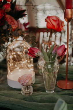 Büyük bir buket, fenerler ve mumlarla süslenmiş yeşil ve kırmızı renklerde bir düğün masasının dekoru..