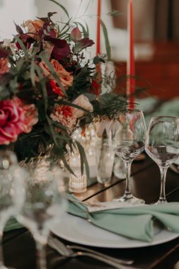 Büyük bir buket, fenerler ve mumlarla süslenmiş yeşil ve kırmızı renklerde bir düğün masasının dekoru..
