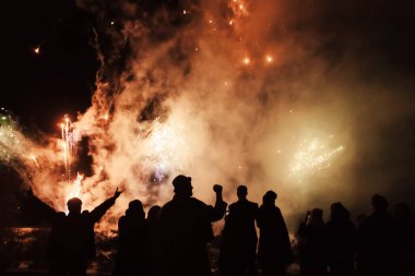 Renkli havai fişeklerin arka planında büyük patlamalarla neşeli insanların silueti..