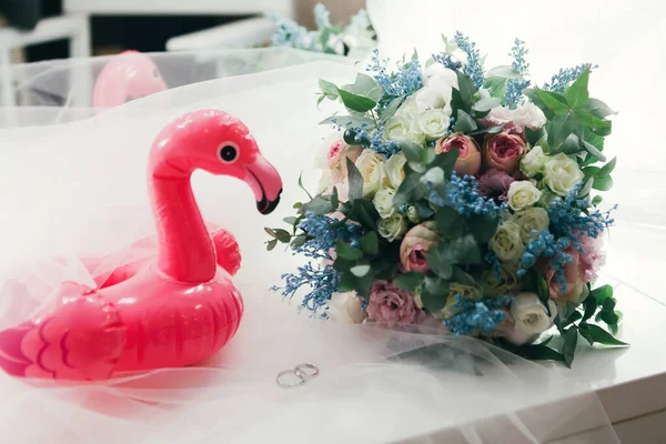 Nikah yüzükleri bir buketin ve şişme bir oyuncağın yanında pembe flamingo şeklinde duruyor..