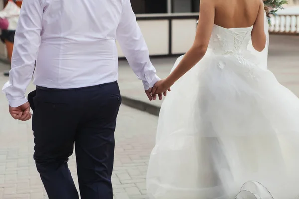 新婚夫妇手牵手沿街走着 新娘的衣服在风中飘扬 — 图库照片
