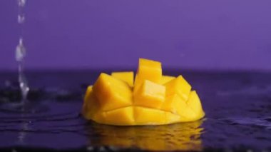 Mor arka planda portakal sulu doğranmış mangoya su sıçratan bir su. makro 180 fps