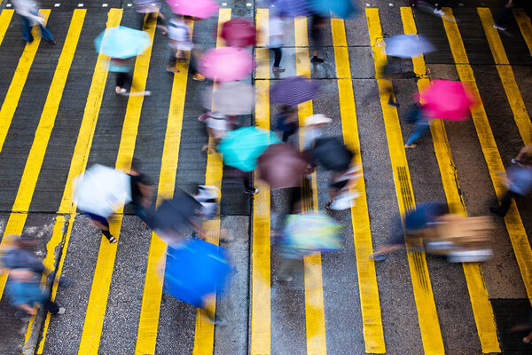 Motion blurred pedestrians crossing Hong Kong street in the rain