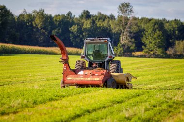 Barron County, WI / USA - 29 Ağustos 2020: Beyaz traktör yaz boyunca yeni kesilmiş samanlıkta bir New Holland helikopterine bağlı, seçici odaklı