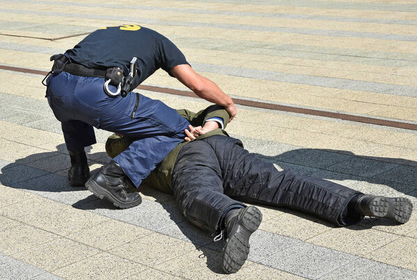Офицер полиции арестовывает преступника на улице

