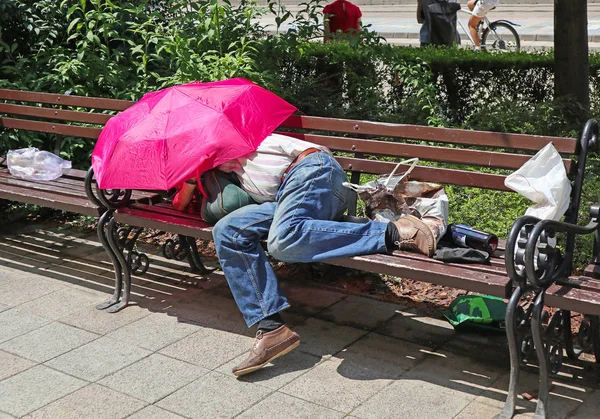 Un vagabundo duerme en un banco de la ciudad. — Foto de Stock