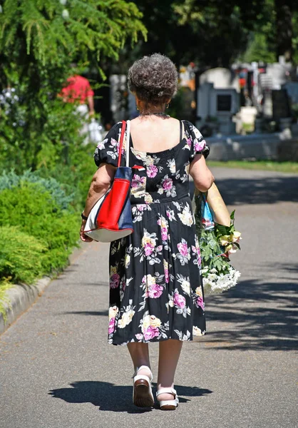 Mulher velha está andando no cemitério com um monte de flor — Fotografia de Stock