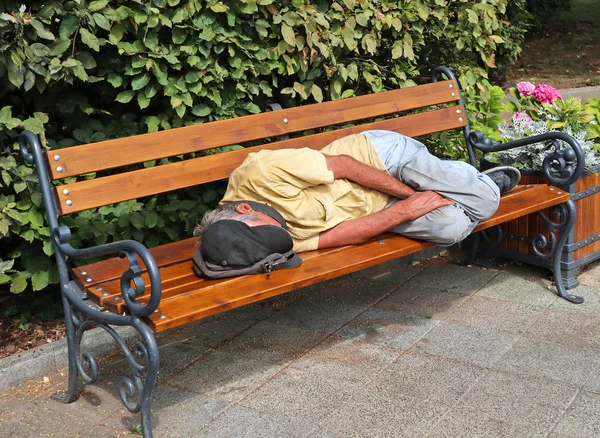 Un vagabundo duerme en un banco del parque. — Foto de Stock