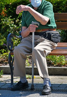 Kıdemli adam maske takmış bir parkta oturuyor.